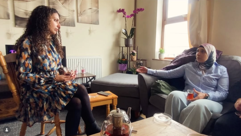 two women, one in a hijab, talking in a living room